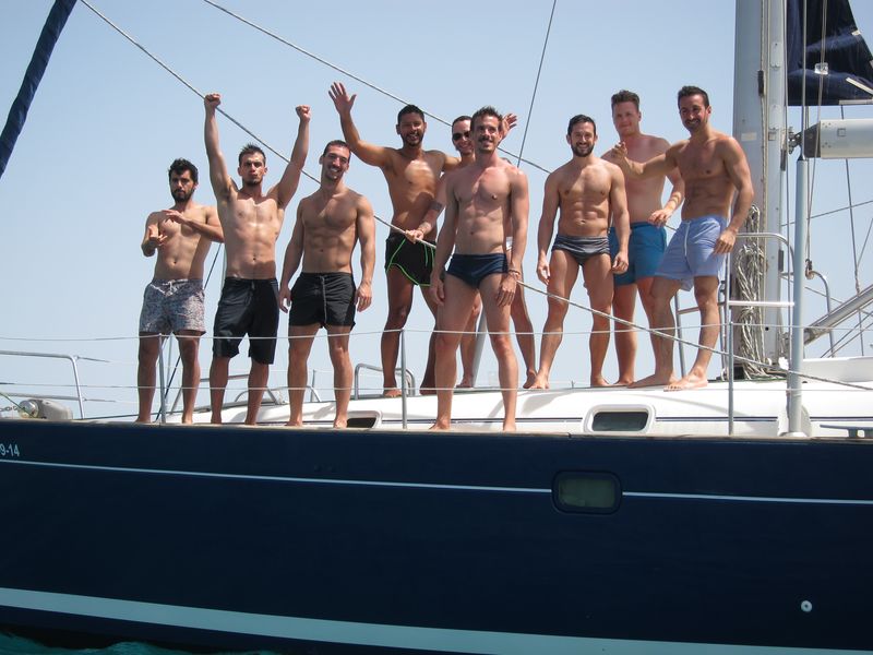 A group of friends enjoy their skippered yacht charter in Ibiza. The guys are on the deck posing in a very funny way.