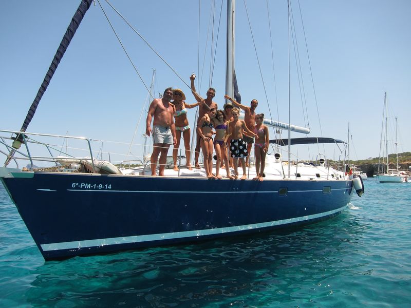 Una familia disfruta de su alquiler de barco en Ibiza con patrón. Varios adultos acompañados de varios niños posan de manera divertida en la cubierta del velero.