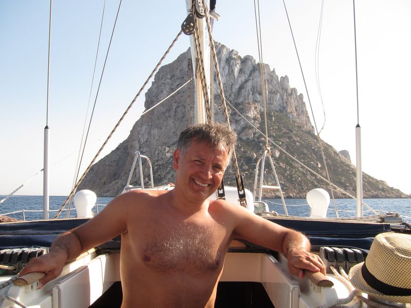 Nuestras excursiones barco Ibiza están llenas de clientes satisfechos. En la imagen se muestra a un cliente sonriente con el islote de Es Vedrà de fondo