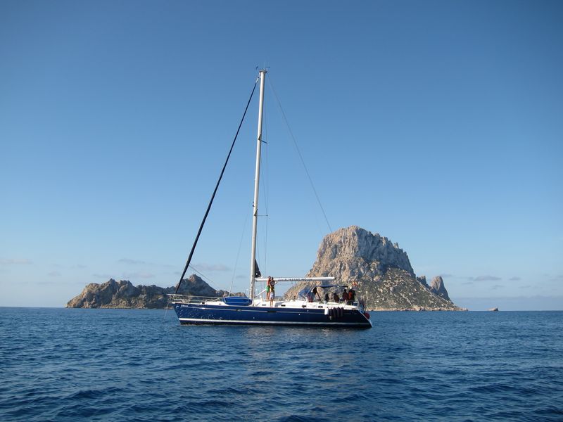 Magnífica Ibiza boat trips en los islotes de Es Vedrà y Es Vedranell. En la imagen puede apreciarse un bello velero de casco azul con los islotes de fondo